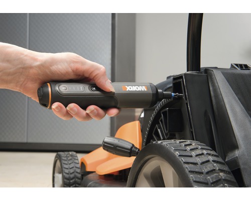 Ruka drží akumulátorový skrutkovač, ktorý sa používa na kosačke na trávu.