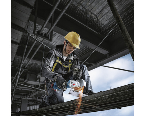 Stavebný robotník s ochrannou prilbou používa uhlovú brúsku na lešení.