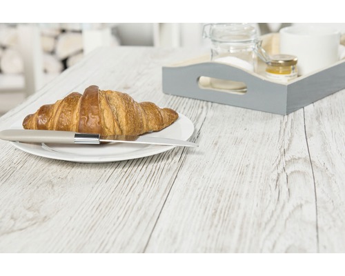 Croissant s nožom na tanieri a raňajková tácka na drevenom stole.