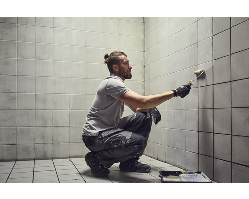 Muž maľuje valčekom na farbu obkladačky v miestnosti.