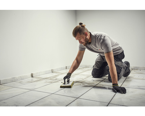 Obkladač čistí dlaždice pomocou špongiovej stierky