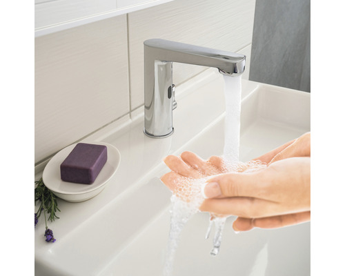 Osoba si umýva ruky pod chrómovanou vodovodnou batériou v umývadle.