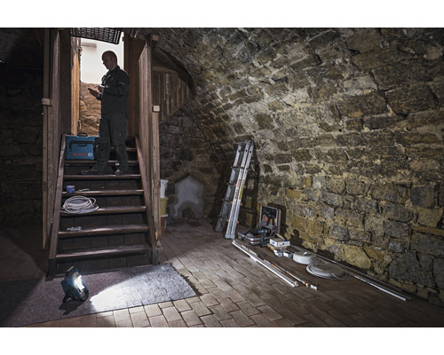 Pivničný priestor s kamenným schodiskom, pracovnou lampou, kufríkom s náradím a remeselníkom