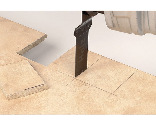 Oscilačná píla reže dlaždicu pozdĺž ceruzkovej čiary.