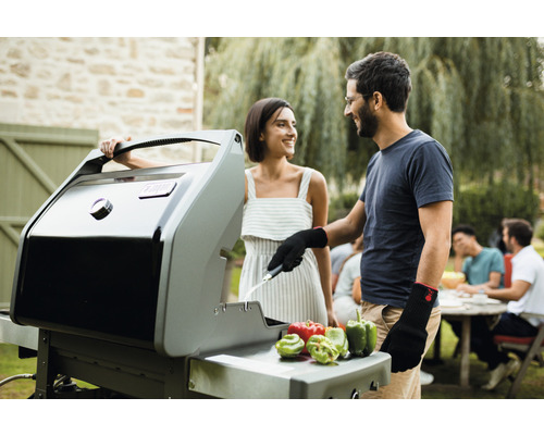 Pár griluje na plynovom grile na záhrade. Na grilovacej ploche ležia papriky.