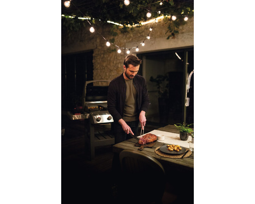 Muž krája mäso na terase s grilom a svetelnou reťazou