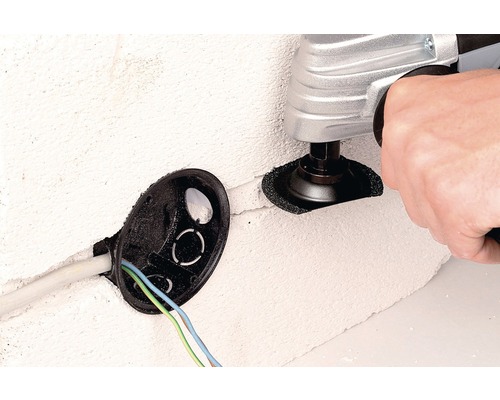 Osoba používa multifunkčný nástroj na vytvorenie výrezu v stene vedľa čiernej rozvodnej krabice.