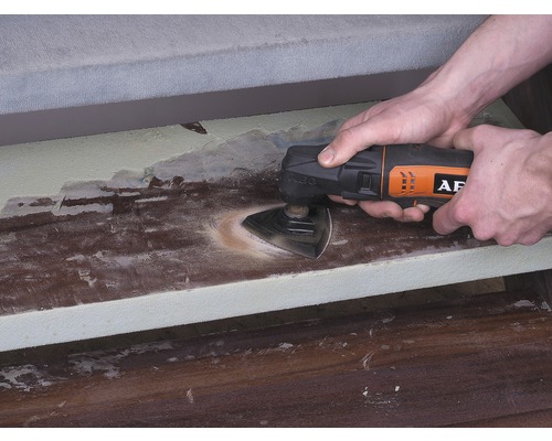 Osoba používa multifunkčný nástroj na brúsenie dreveného povrchu. Logo AEG.