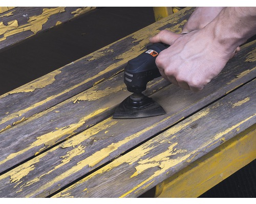 Osoba používa multifunkčný nástroj na brúsenie farby na drevenej lavici.