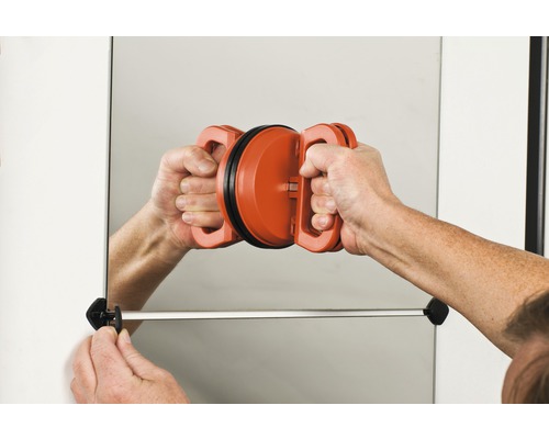 Osoba montuje zrkadlo na stenu pomocou prísavky