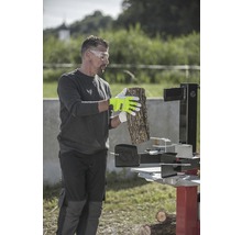 Muž s ochrannými okuliarmi, pracovnými rukavicami a štiepačkou na drevo spracováva drevo