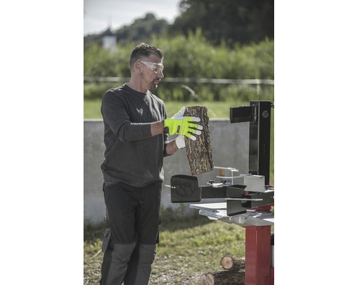 Muž s ochrannými okuliarmi, pracovnými rukavicami a štiepačkou na drevo spracováva drevo