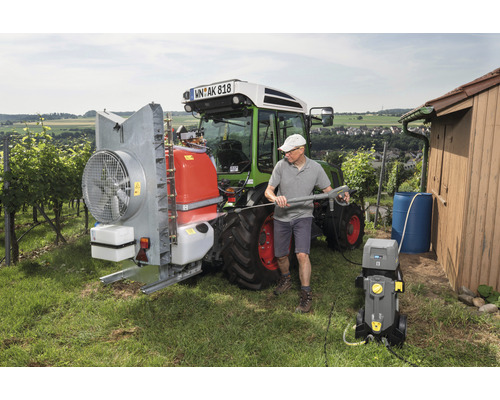Muž čistí traktor vysokotlakovým čističom vo vidieckom prostredí.
