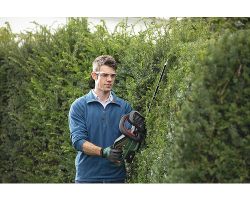 Muž strihá živý plot akumulátorovými nožnicami na živý plot v záhrade.
