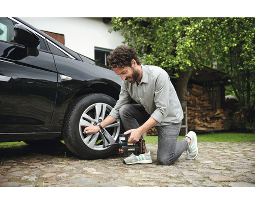 Muž hustí pneumatiku auta pomocou akumulátorového kompresora