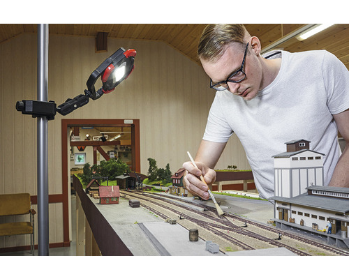 Muž pracuje na modelovej železnici pod pracovným svetlom.