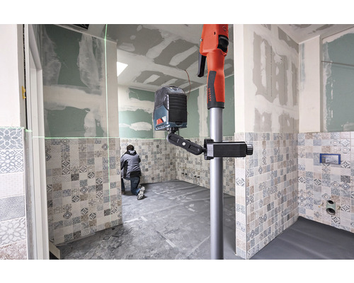 Pracovník používa čiarový laserový nivelačný prístroj so statívom v kúpeľni s obkladmi.