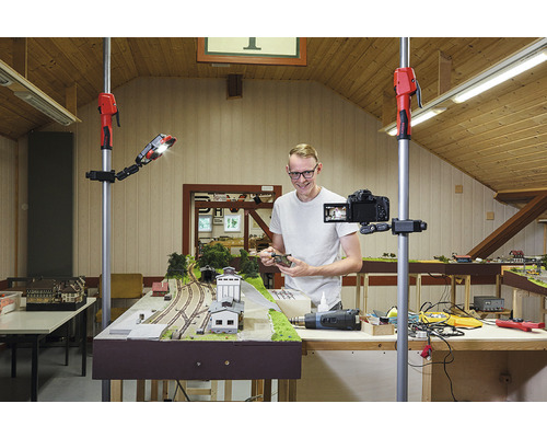 Muž natáča modelovú železnicu kamerou na statíve a pracovným svetlom.