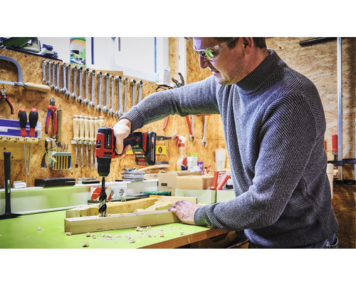 Muž vŕta dieru do drevenej dosky akumulátorovou vŕtačkou v dielni.