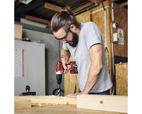 Remeselník vŕta akumulátorovým vŕtacím skrutkovačom otvor do drevenej dosky