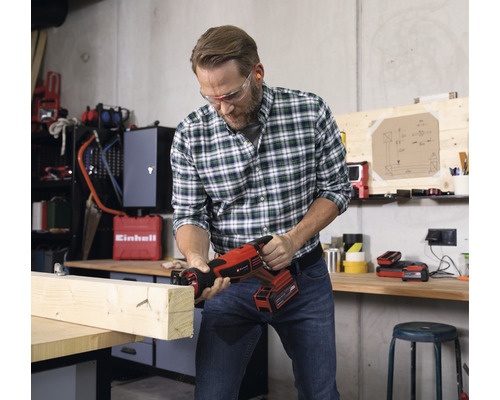 Muž pília drevenú dosku akumulátorovou šabľovou pílou v dielni.