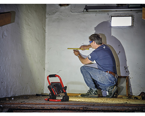 Muž meria stenu skladacím metrom, priestor osvetľuje stavebný reflektor