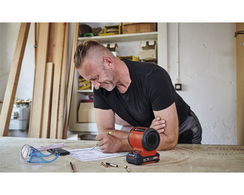 Muž pracuje na stavebnom pláne s akumulátorovou lampou Einhell na stole.