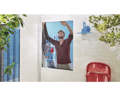 Muž montuje sieť proti hmyzu na okno.