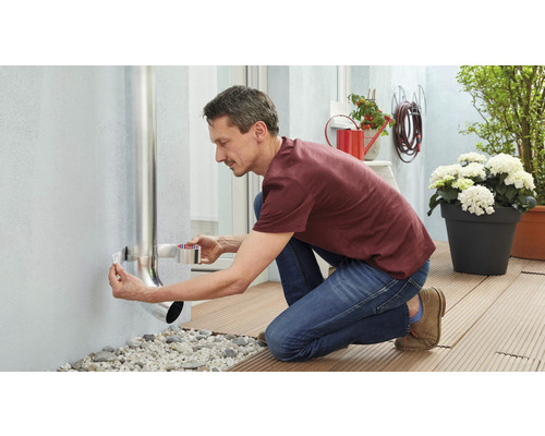 Muž upevňuje dažďovú rúru k domovej stene pomocou tesniacej pásky.