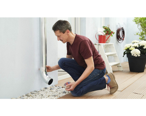 Muž pripevňuje odkvapovú rúru na vonkajšiu stenu domu.