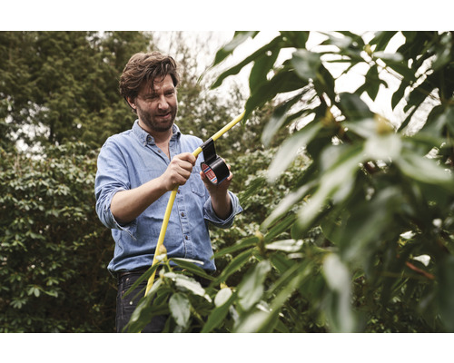 Muž opravuje žltú hadicu čiernou izolačnou páskou v záhrade.