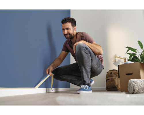 Muž lepí maskovaciu pásku na stenu v miestnosti