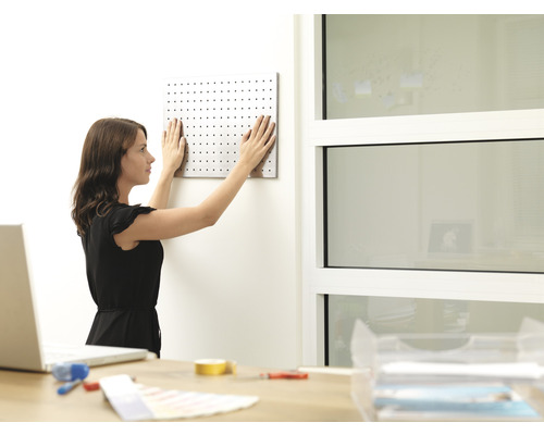 Žena upevňuje dierovaný panel na stenu v kancelárii.