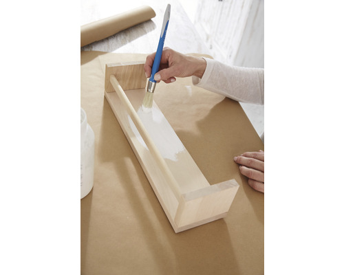 Osoba natiera drevenú policu bielou farbou štetcom.