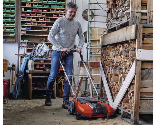 Muž používa akumulátorový zametač v dielni na upratovanie pilín.