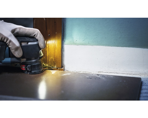 Osoba používa multifunkčnú brúsku na brúsenie drevenej zárubne.