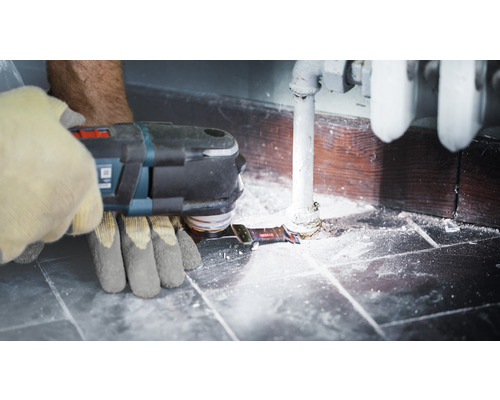 Osoba používa multifunkčný nástroj na vykurovacej trubke blízko steny.