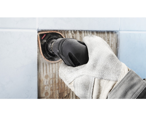 Ruka s ochrannou rukavicou odstraňuje dlaždice pomocou multifunkčného nástroja