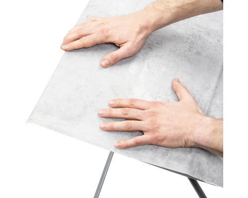 Muž pripevňuje nábytkovú fóliu na povrch.