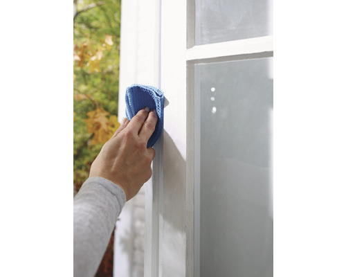 Osoba čistí okno modrou handričkou z mikrovlákna