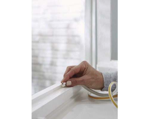 Osoba pripevňuje tesniacu pásku k rámu okna.