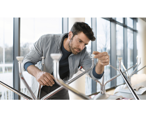 Muž montuje vešiak na šaty s kovovým rámom a bielymi plastovými dielmi.