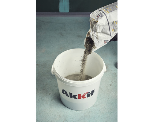 Osoba sype suchú betónovú zmes z vreca do vedra.