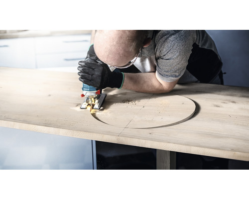 Muž vyrezáva otvor do drevenej dosky pomocou priamočiarej píly.