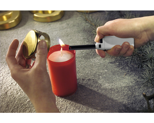 Osoba zapaľuje sviečku tyčovým zapaľovačom. Viečko sviečky je držané v ruke.