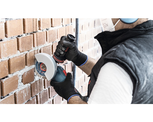 Remeselník reže tehlovú stenu uhlovou brúskou