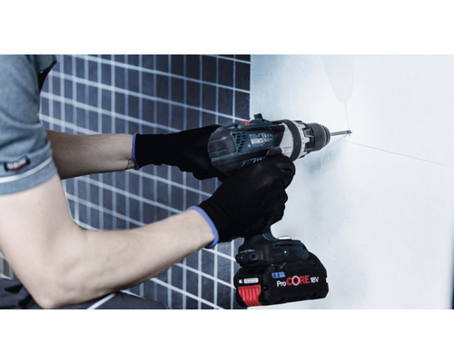 Muž vŕta vŕtačkou dieru do steny.