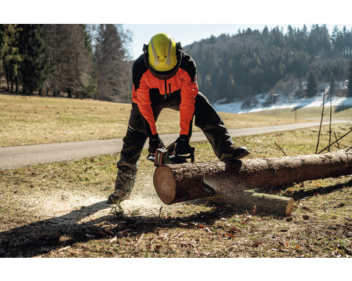 Osoba v ochrannom odeve reže kmeň stromu motorovou pílou.
