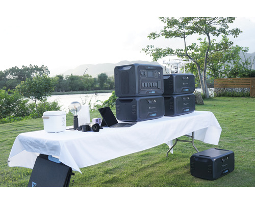 Snímka vonkajšej scény s niekoľkými prenosnými elektrárňami Bluetti na stole spolu s rôznymi zariadeniami