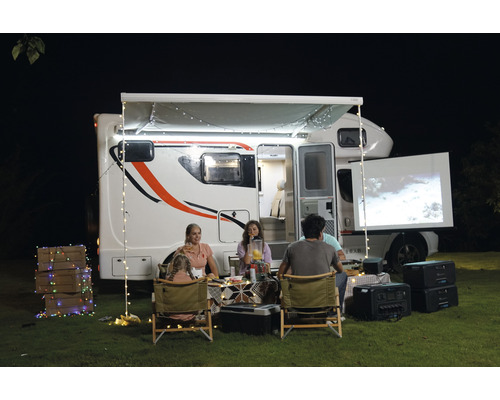 Rodina si užíva filmový večer vonku s obytným vozidlom, projektorom a plátnom.
